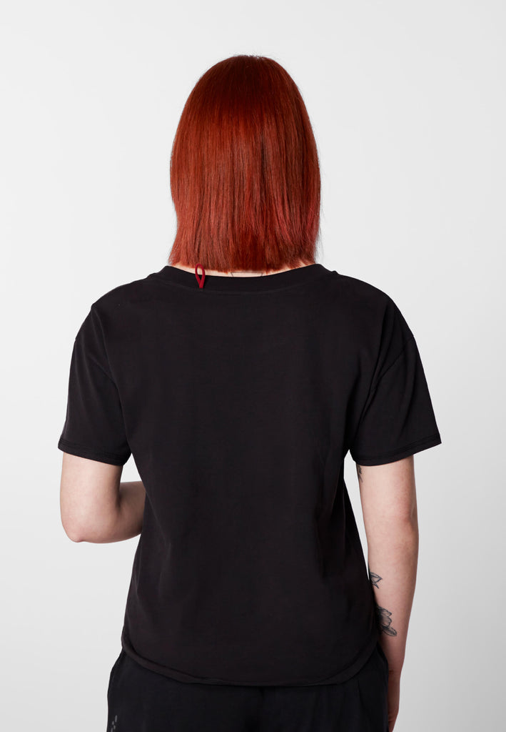 Rückansicht einer Frau im Pyjama T-Shirt in der Farbe „night black“.