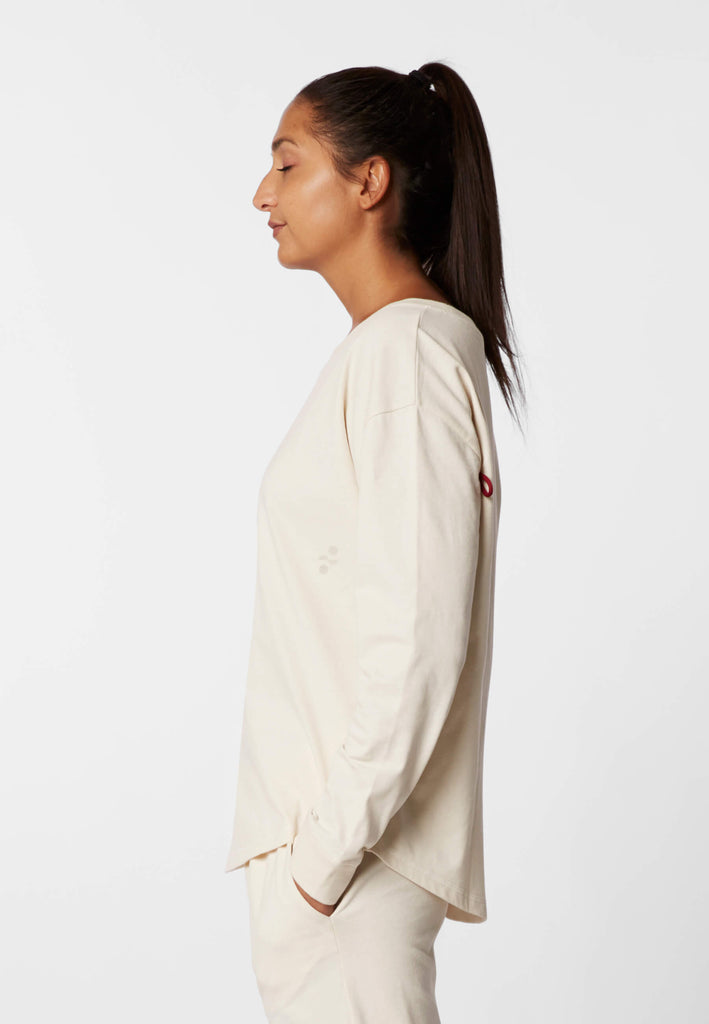 Seitenansicht einer Frau im Pyjama Longsleeve in der Farbe „moon white“.