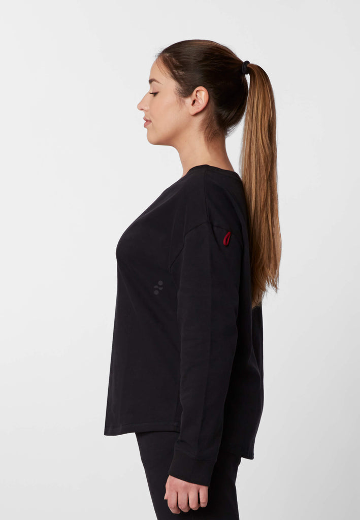 Seitenansicht einer Frau im Pyjama Longsleeve in der Farbe „night black“.