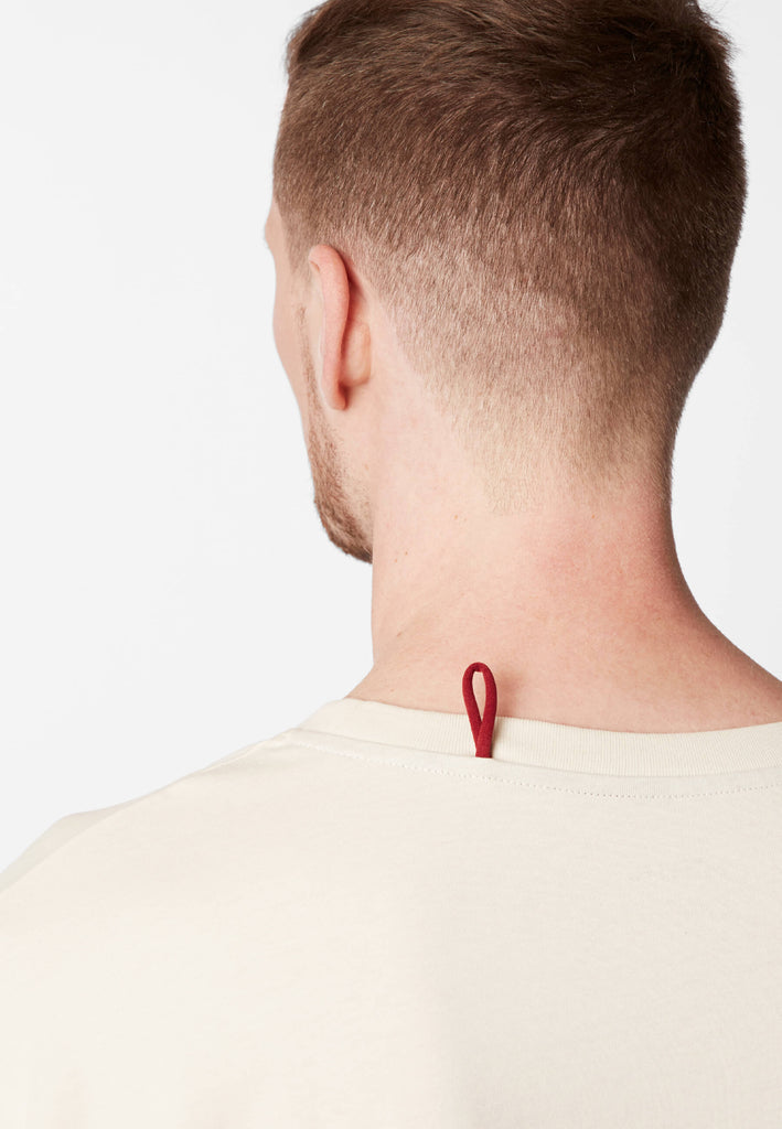 Detailbild einer roten Schlaufe am Pyjama T-Shirt in der Farbe „moon white“ an der Nackennaht.