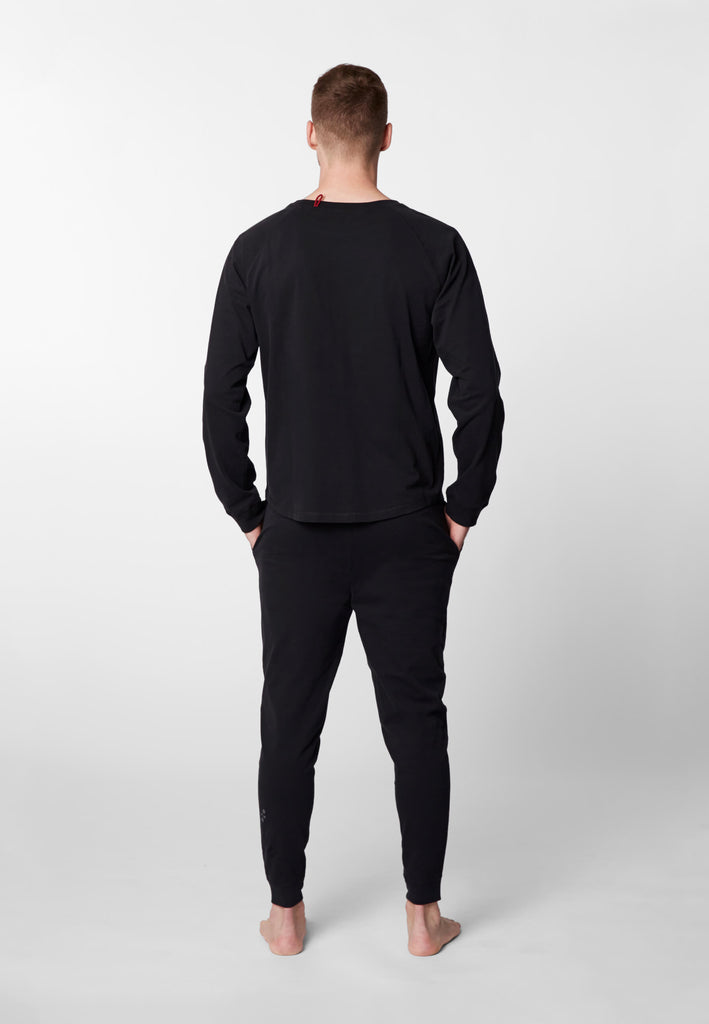 Ganzkörper Rückansicht eines Mannes im Pyjama Longsleeve und Pyjamahose in der Farbe „night black“.