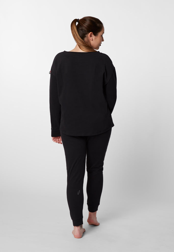Ganzkörper Rückansicht einer Frau im Pyjama Longsleeve und Pyjamahose in der Farbe „night black“.