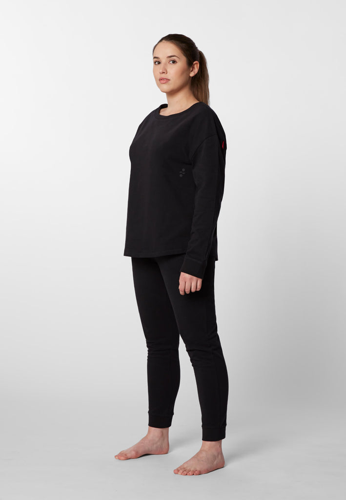 Ganzkörper Vorderansicht einer Frau in einer Pyjamahose und eines Pyjama Longsleeves in der Farbe „night black“.