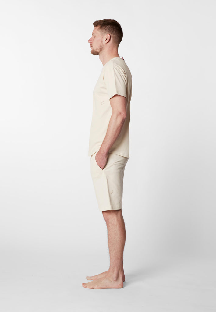 Ganzkörper Seitenansicht eines Mannes in einer Pyjama Shorts und einem Pyjama T-Shirts in der Farbe „moon white“.